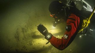 Close up of a scuba diver in deep dark water using their torch to inspect a sunken vessel.