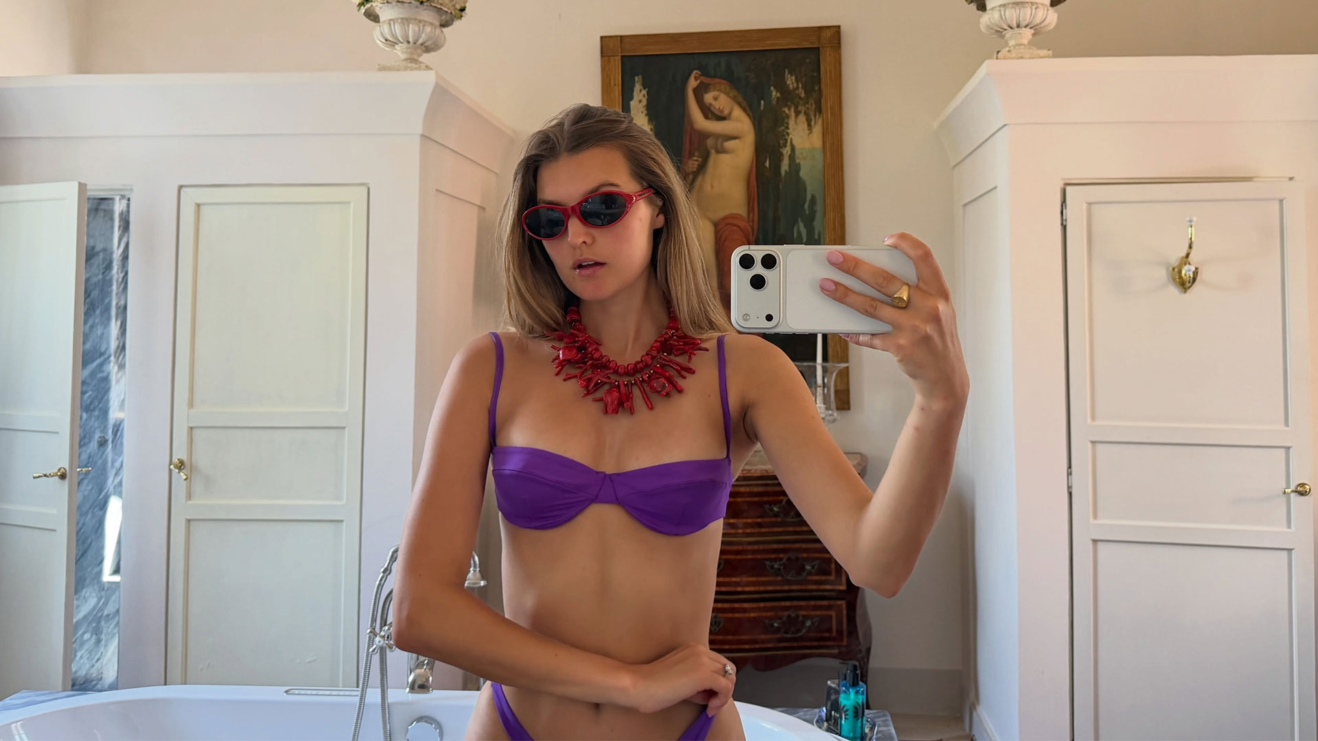 @styledsara wearing a purple bikini with a red coral statement necklace.