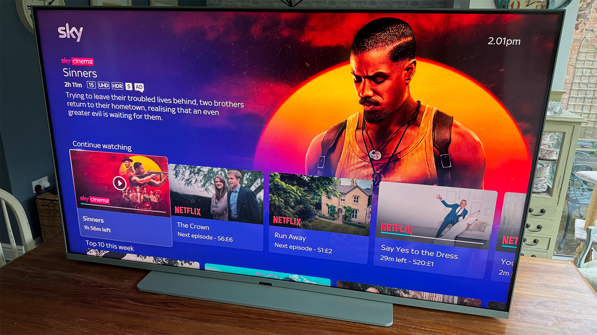 Sky Glass Air 4K TV on wooden dining table, on screen is Sky OS highlighting Sinners