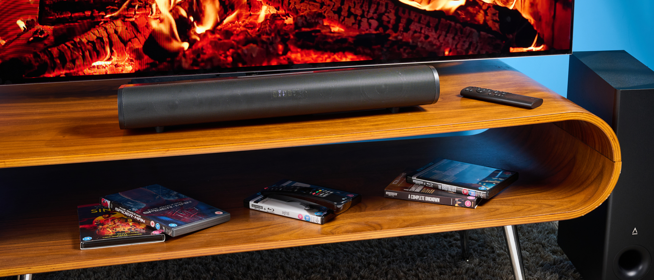 the creative stage pro soundbar and subwoofer, a super-budget home cinema system with 2.1 channels and a remote control photographed on a wooden tv stand with a TV behind