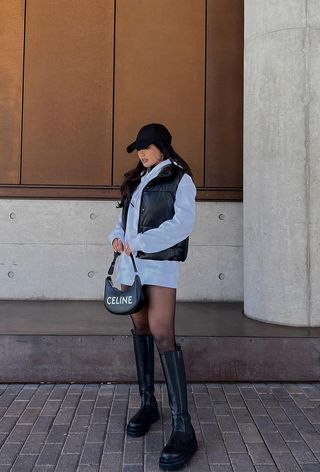 a roundup of the best puffer jackets shown in a photo of a woman wearing a a puffer vest over an oversized sweatshirt styled as a dress worn with knee-high flat boots