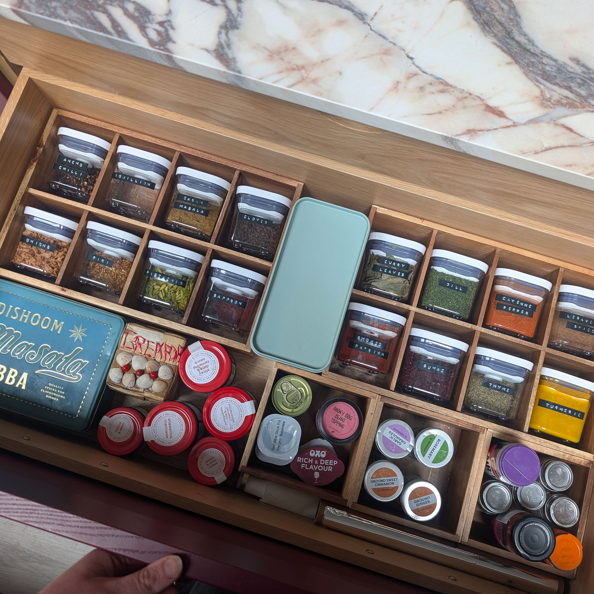 Open drawer showing herbs and spices organised into storage containers and wooden divided drawer sections