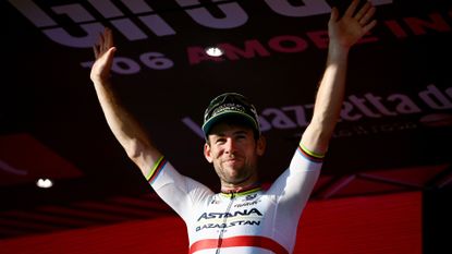 Mark Cavendish in a cap, waving to the crowds from the stage after winning stage 21 of the 2023 Giro d'Italia