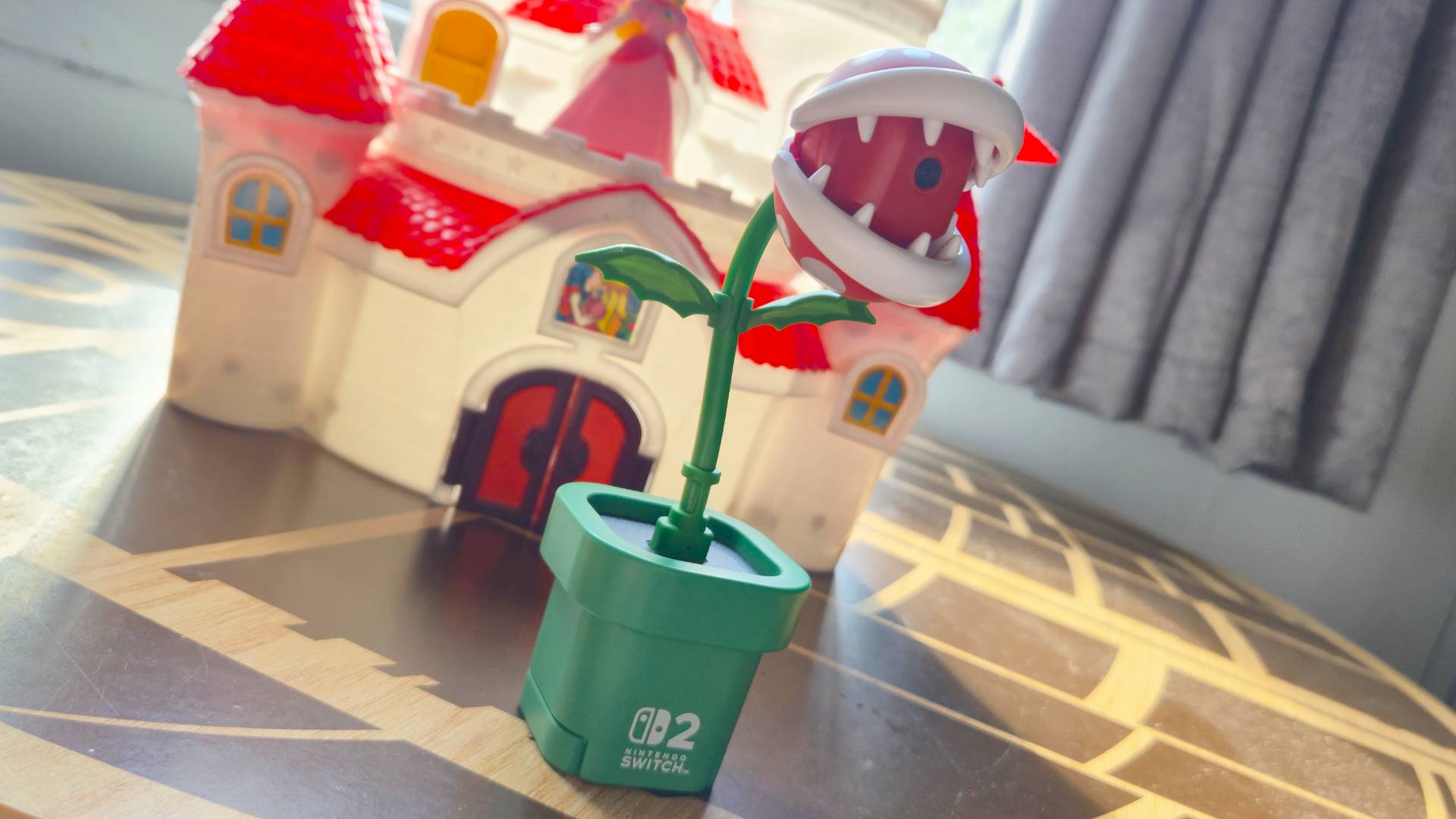 Photo by Rosalie Newcombe of the Hori Piranha Plant Switch 2 camera sitting in front of a Super Mario Peach Castle toy set.