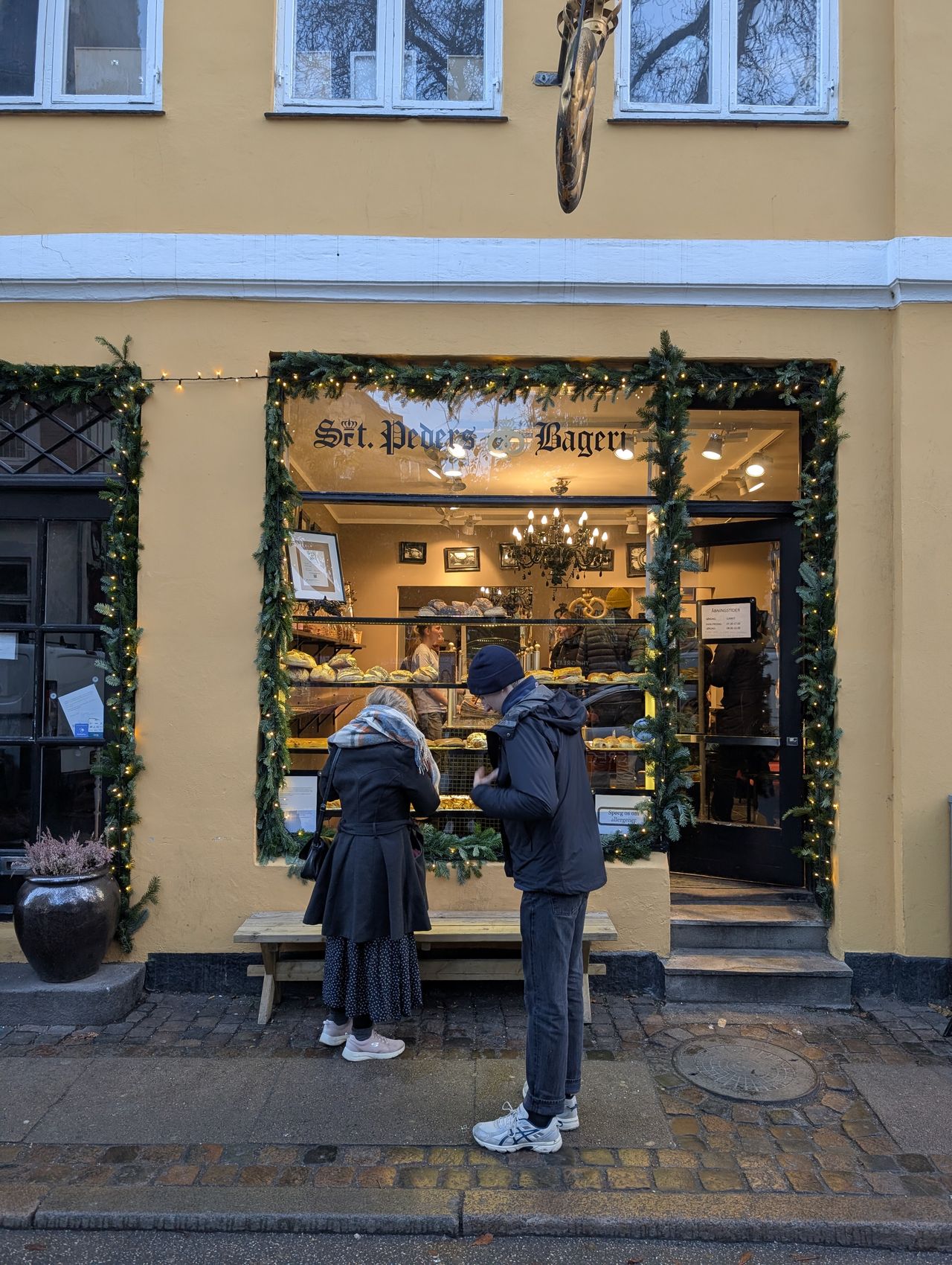 Two people outside a bakery window decorated for christmas