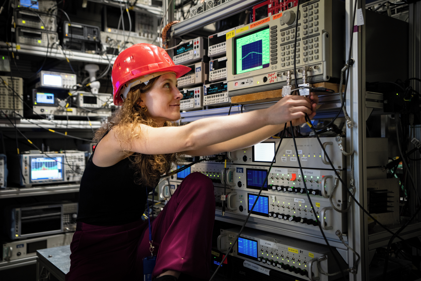 A woman wearing a hard hat works on a control panel