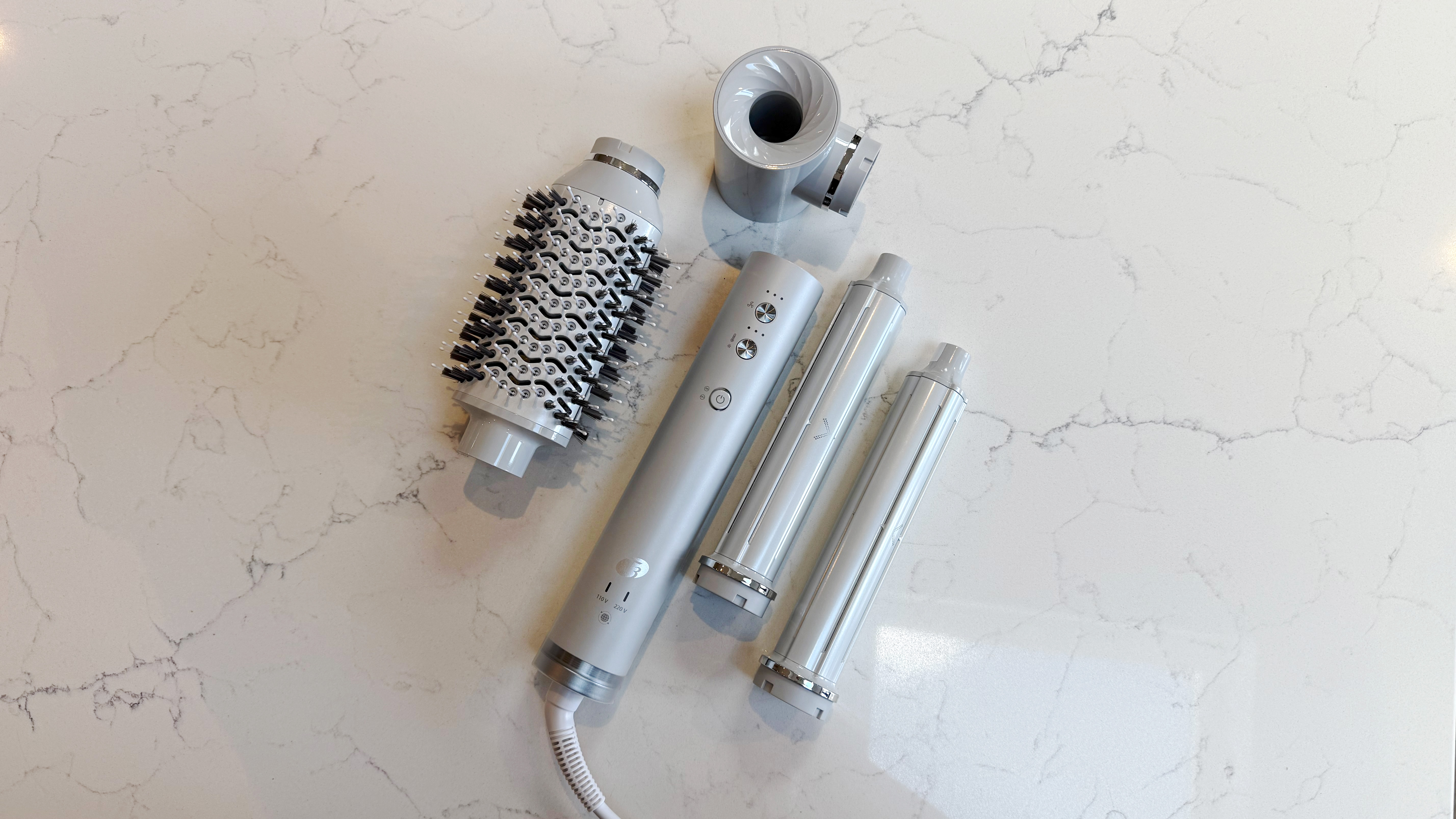 Top-down view of the T3 Aire 360 and attachments: oval brush top left, SoftAire concentrator top right, two ceramic curling barrels to the right, base in the centre