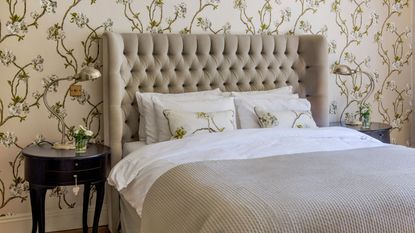 Master bedroom with a double bed and matching side tables, padded headboard and floral wallpaper.