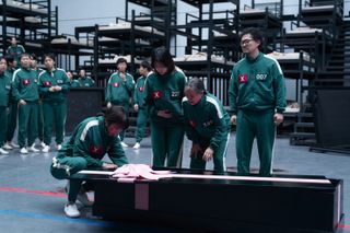 Hyun-ju (Park Sung-hoon), Jun-hee (Jo Yu-ri), Geum-ja (Kang Ae-shim), and Yong-sik (Yang Dong-geun) lean over an open gift-wrapped coffin as other players crowd behind them to the left, in 'Squid Game' season 3.