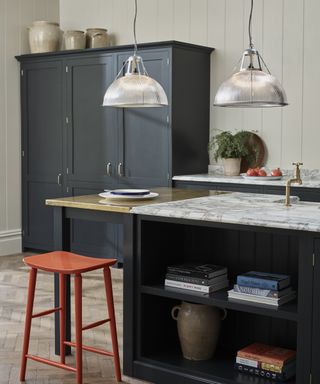 Blue, black and white kitchen with navy freestanding cabinet, black kitchen island with marble and copper top, red barstool, glass pendant lights
