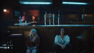 Nicola Coughlan and Lydia West sitting on the floor in the bar in Big Mood. 