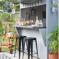 grey shed set up as outside bar with bar stools, on a patio beside the lawn, party sign and cocktail bar