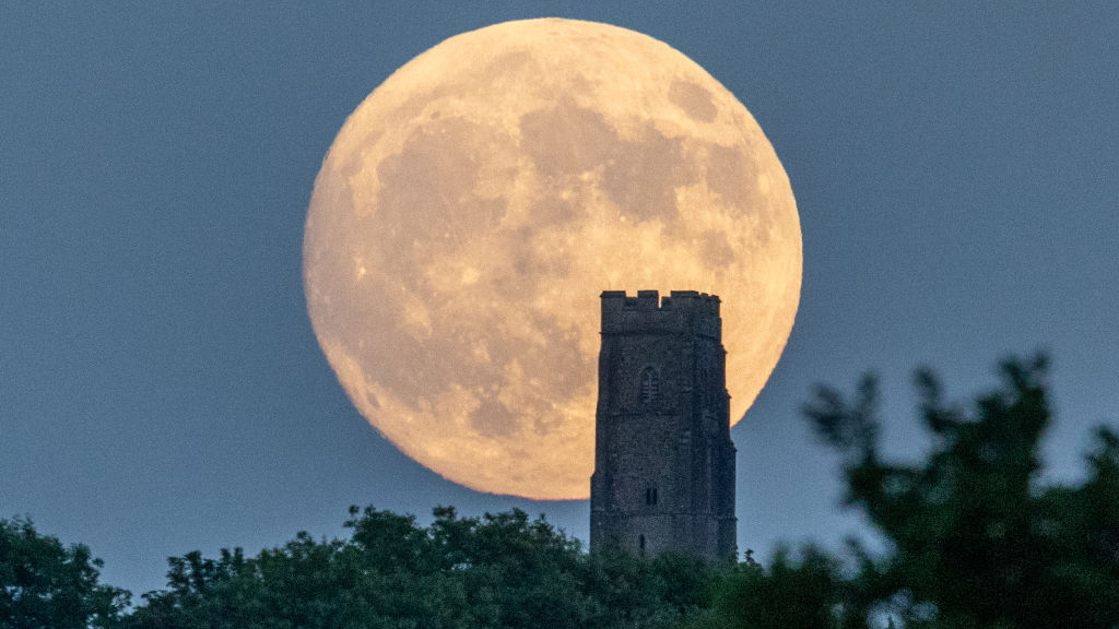 GLASTONBURY, UNITED KINGDOM - JUNE 13: People gather as a strawberry supermoon rises behind Glastonbury Tor on June 13, 2022 in Glastonbury, England. Tonight's supermoon, so called because it is one of the closest full moons to the Earth this year, is also known as a strawberry moon. (Photo by Matt Cardy/Getty Images)