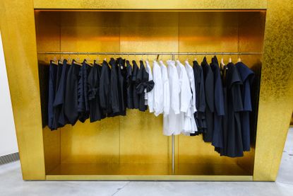 Best fashion stores New York: inside of Comme des Garçons Chelsea with clothes arranged on rail with gold backdrop
