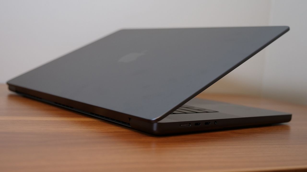 A laptop with its lid half-closed angled away from the camera on a wooden desk