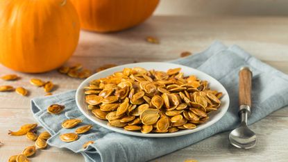 Plate of roasted pumpkin seeds with small pumpkins in background