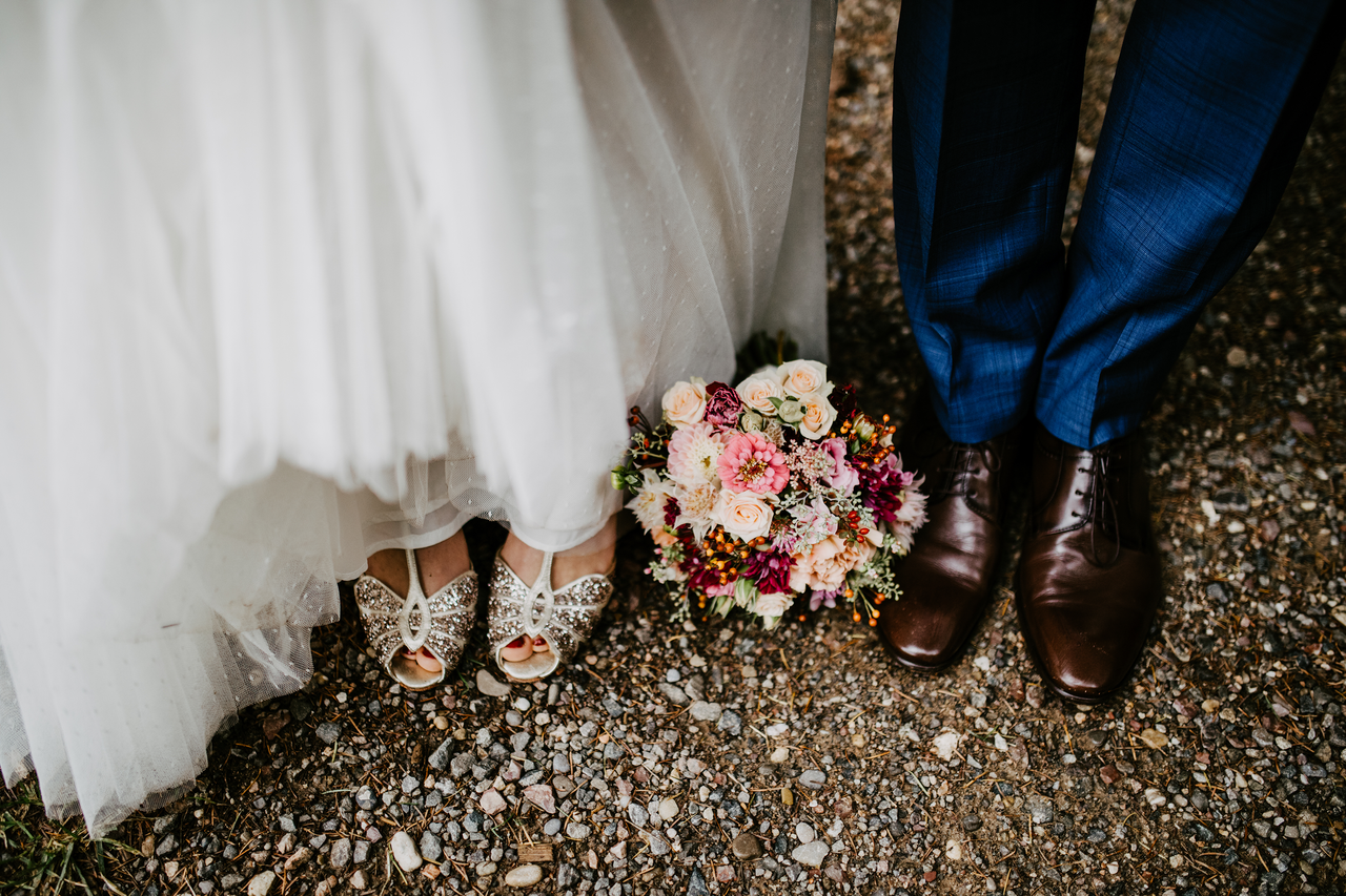 A close up of a bride&#039;s dress and a groom&#039;s shoes