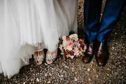 A close up of a bride's dress and a groom's shoes