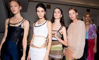 Models wear dark blue and black dress, white top and skirt, beige and brown dress, and light pink jumper