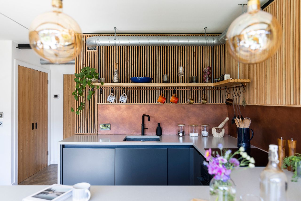 A small kitchen with modern wood panelling and a copper colour kitchen splashback