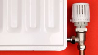 Close up of a white radiator and TRV (Thermostatic Radiator Valve) on red background