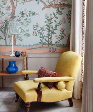 traditional style yellow arm chair against a pale blue wall mural with a leaf and tree pattern