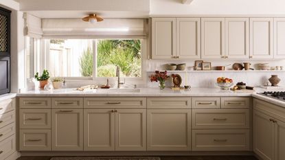 a neutral kitchen with light tan painted cabinets, decor on the countertops, and a large window above the sink 
