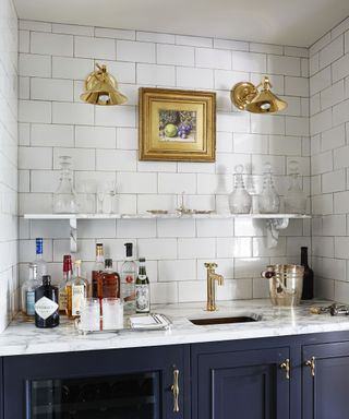 A kitchen bar alcove with marble counter, brass wall sconces, brass faucet and navy cabinetry