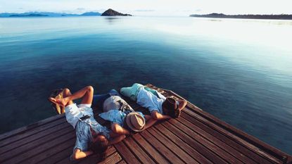 Three men kick back and relax on a dock at a lake