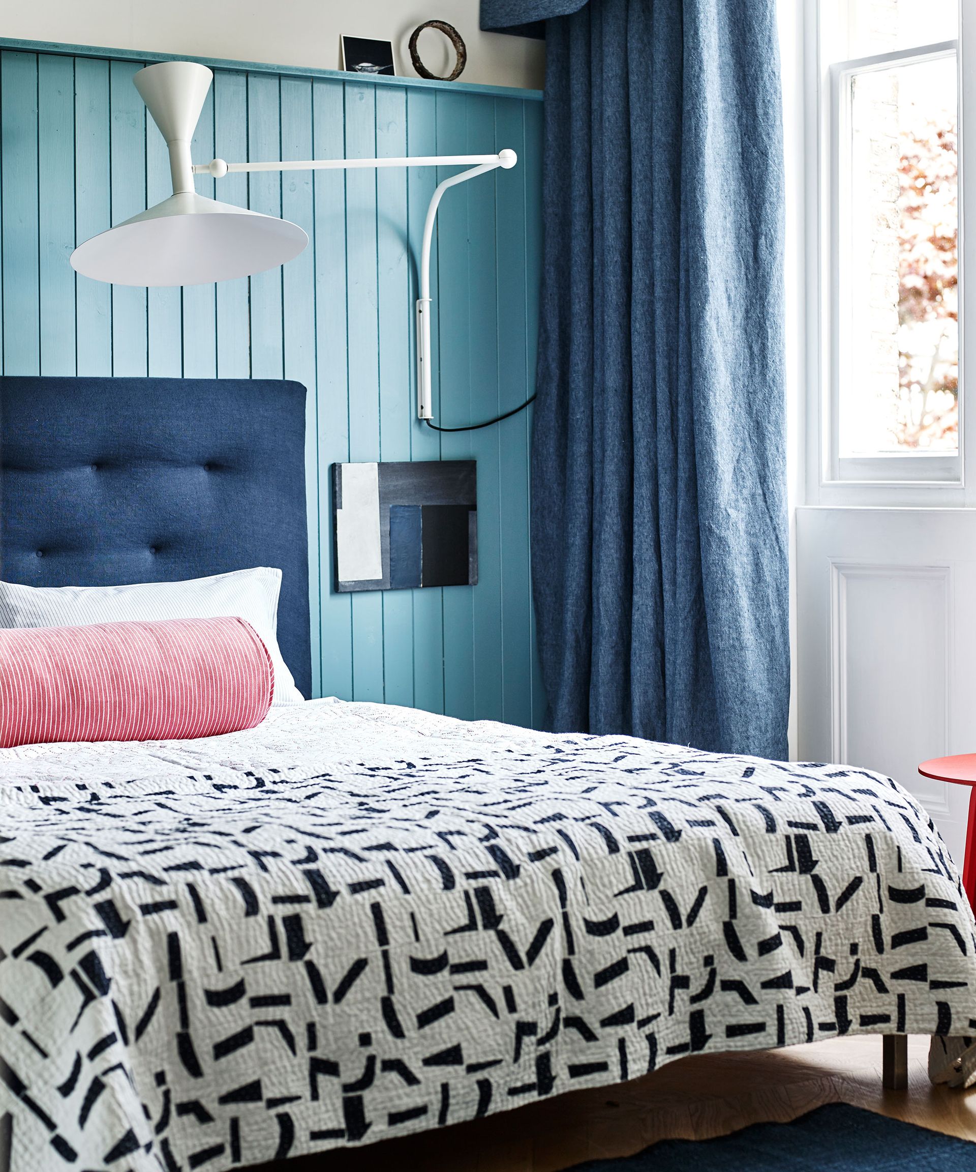 An example of guest room ideas showing a blue paneled wall behind a bed with a navy blue headboard and a monochrome throw