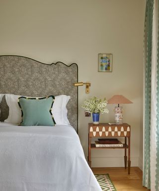 neutral bedroom with green accents including a patterned shaped headboard, thow pillows and striped curtains