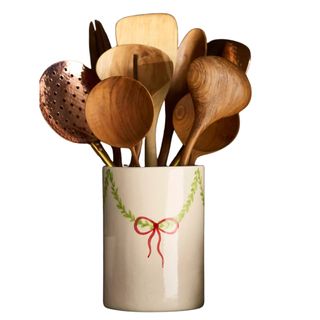 A white ceramic utensil holder with vine and bow detail filled with wooden and copper utensils