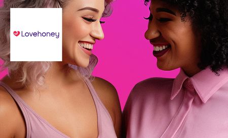 Two women wearing pink getting photographed posing next to each other and laughing