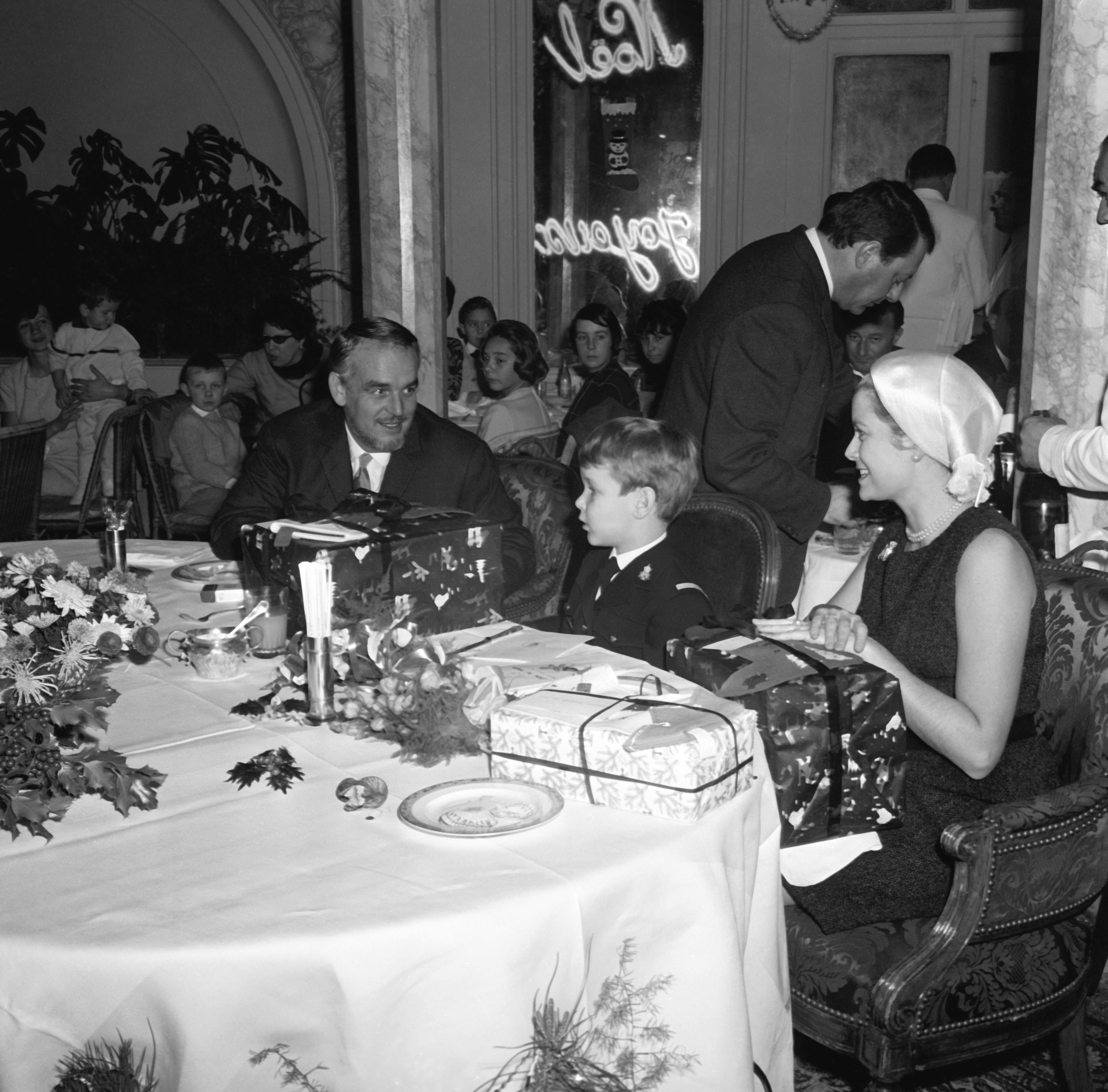 Prince Rainier, Grace Kelly and Prince Albert sitting at a table at a Christmas party in 1965