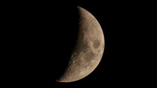An image of the moon close to its first quarter phase, with most of its right-hand side lit by direct sunlight. Dark lunar seas can be seen close to the equator.