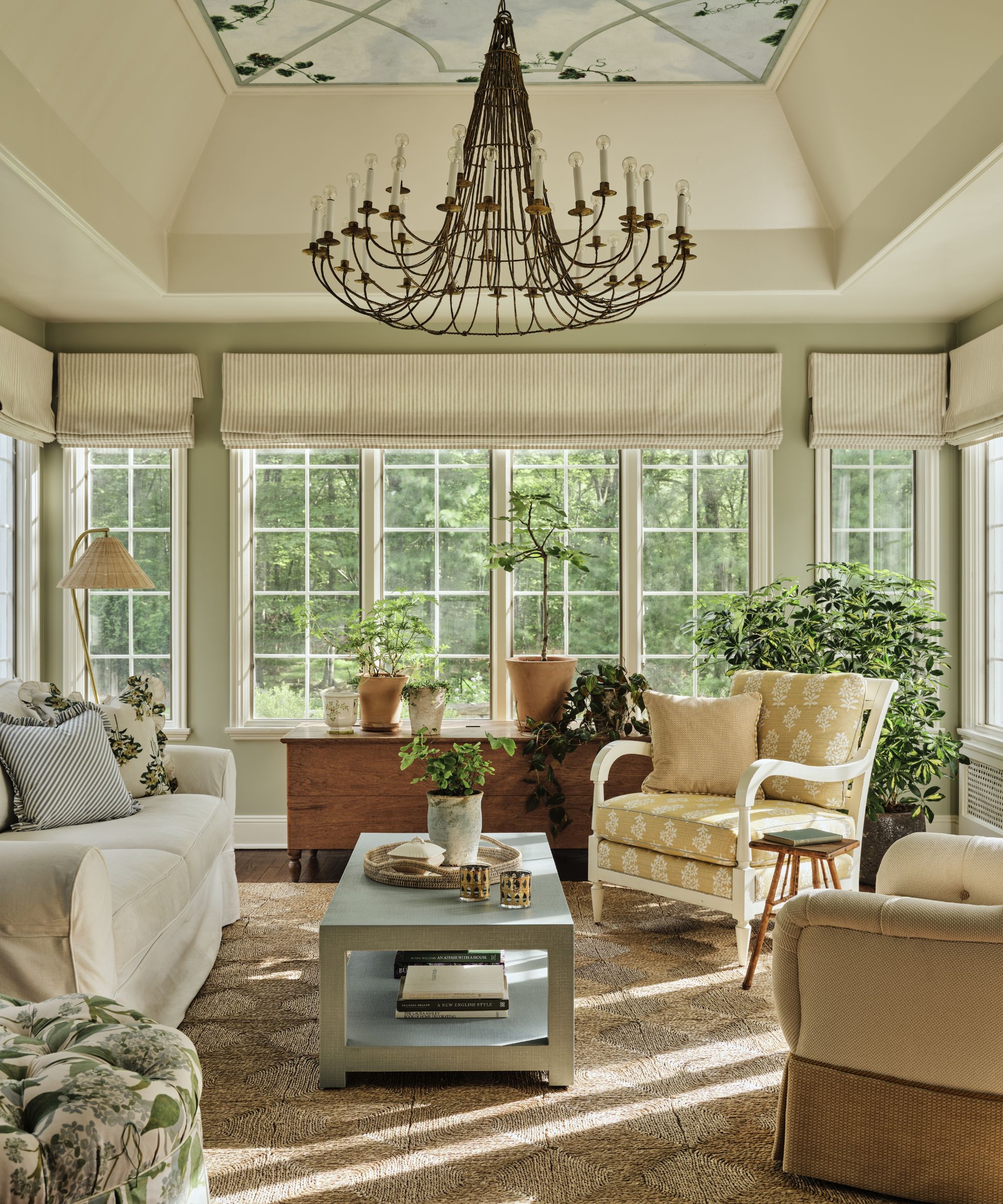 a soft neutral sunroom with a mural ceiling, large chandelier, and english style furniture with floral patterns and a woven rug