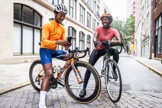 Young cyclist using smartphones in urban environment on a bike with a friend smiling