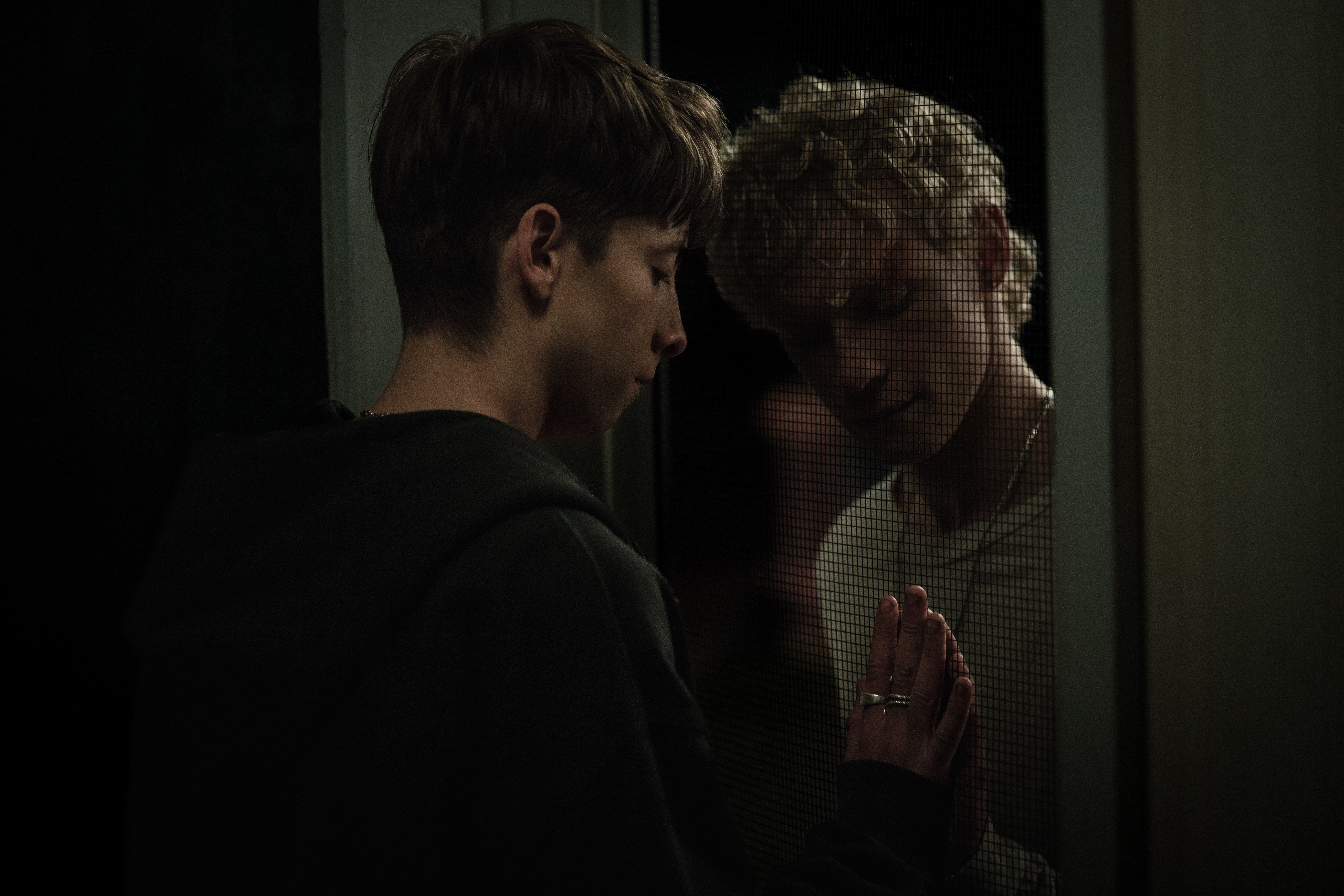 two teenage boys touching hands through a door at night in a still from the horror movie leviticus
