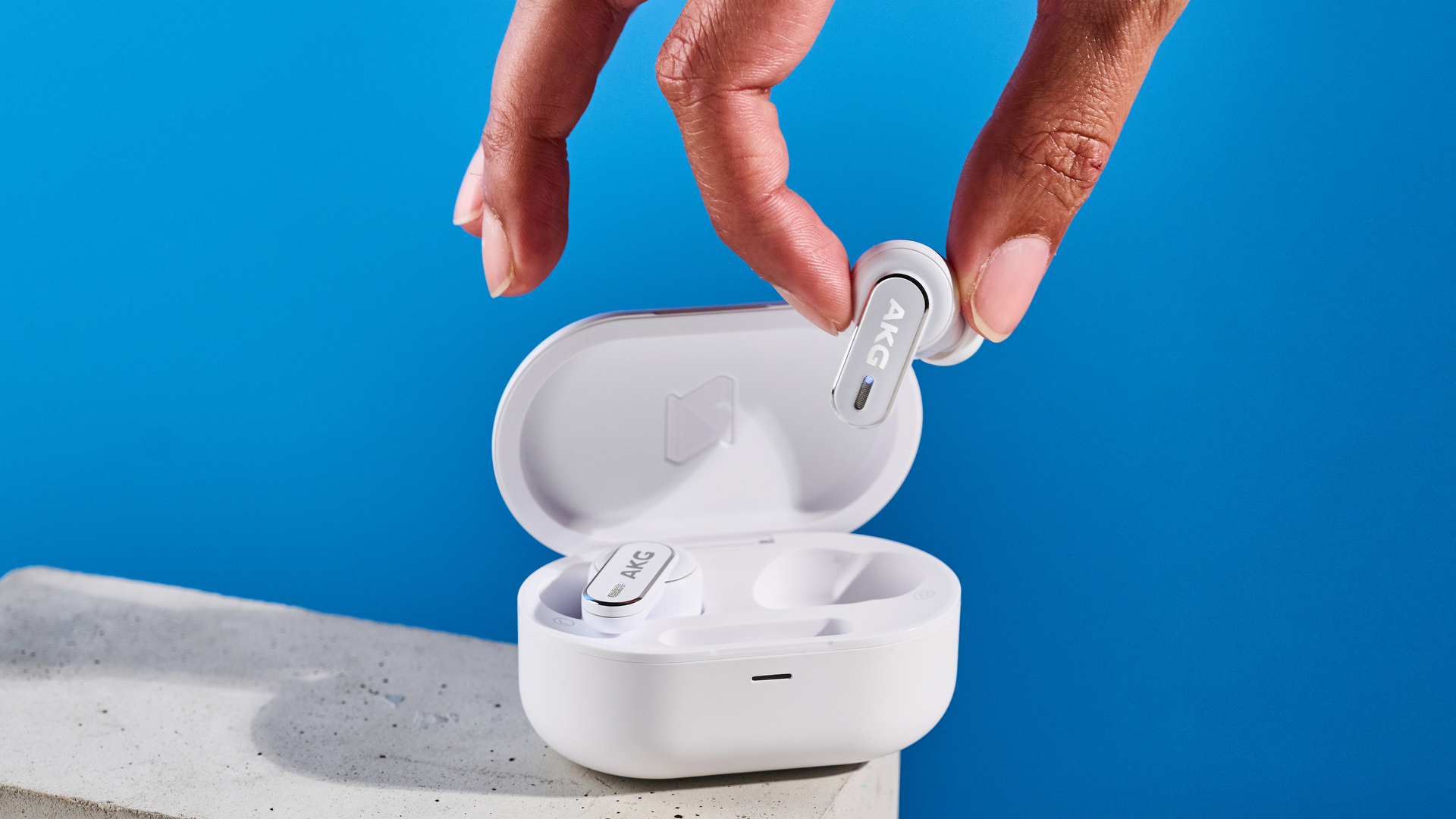 the akg n5 hybrid earbuds by harman in white, shown in their charging case with accessories and without
