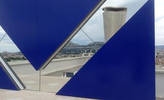 In the distance, A closer look at a wide and tall, square-shaped structure, in deep blue, with a rhombus-shaped mirror.