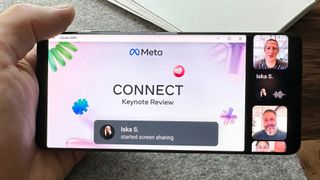 Una mano sostiene un teléfono mostrando una presentación de Meta en una videollamada de WhatsApp con Mark Zuckerberg