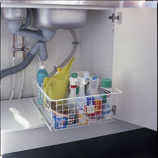White basket with cleaning supplies stored under sink