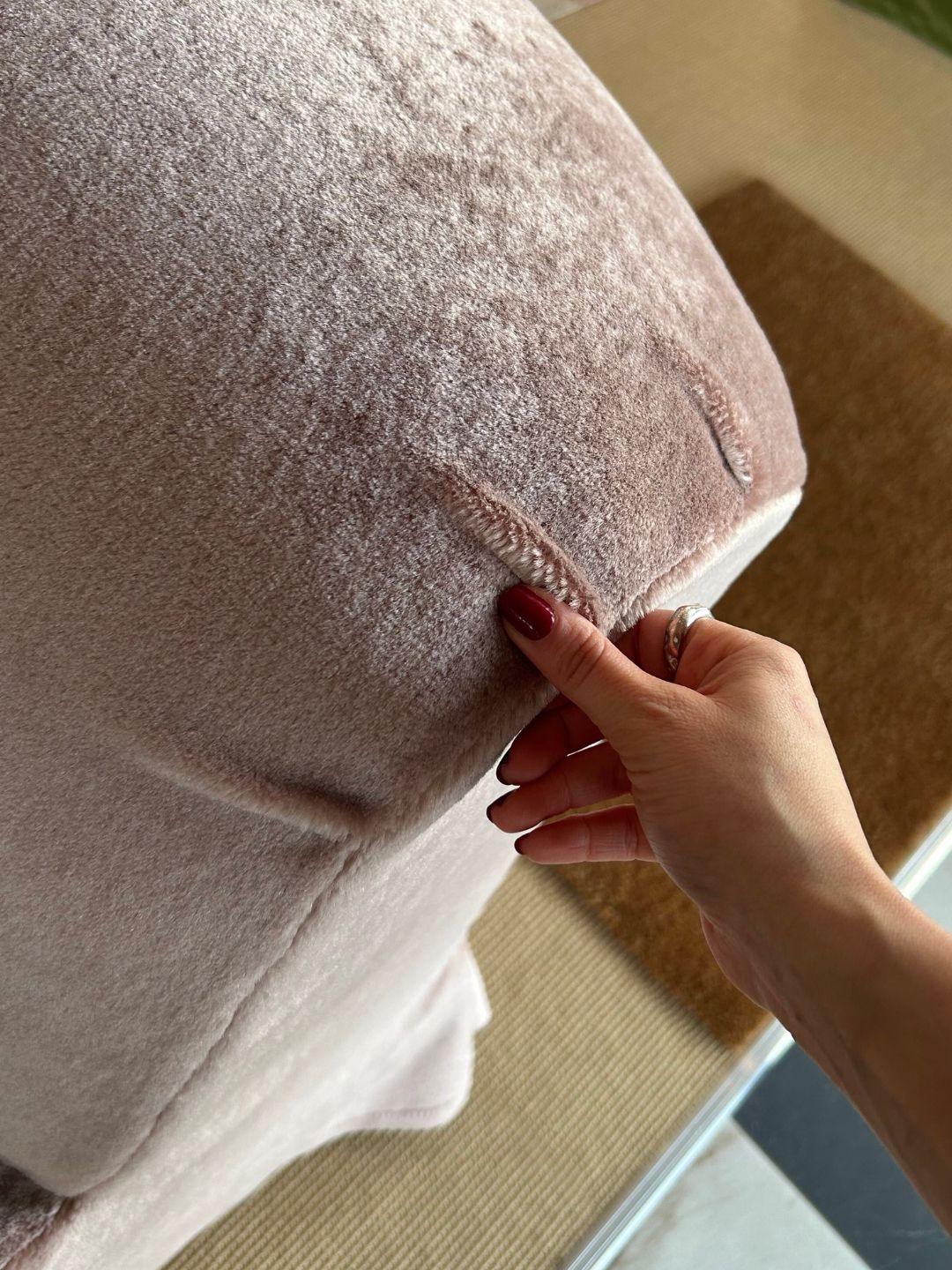 Close-up of a hand pinching the piped edge of a Heather Mohair Velvet cushion on Schplendid's Lenny sofa, showing the plush fabric texture and stitching.