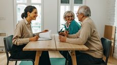 A smiling adviser and her older clients, also smiling, sit at a table. 