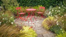 red bistro table and chairs on a circular patio surrounded by planting and ornamental grasses