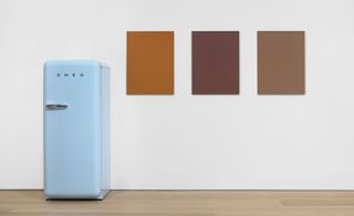 Pastel Blue SMEG Refrigerator on display against a white wall featuring 3 plain coloured (shades of brown) wall arts
