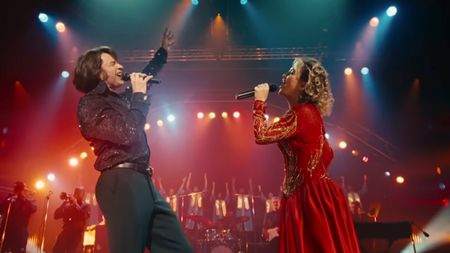 Hugh Jackman on the left holding his arm up and singing with Kate Hudson on the right singing in a red dress.