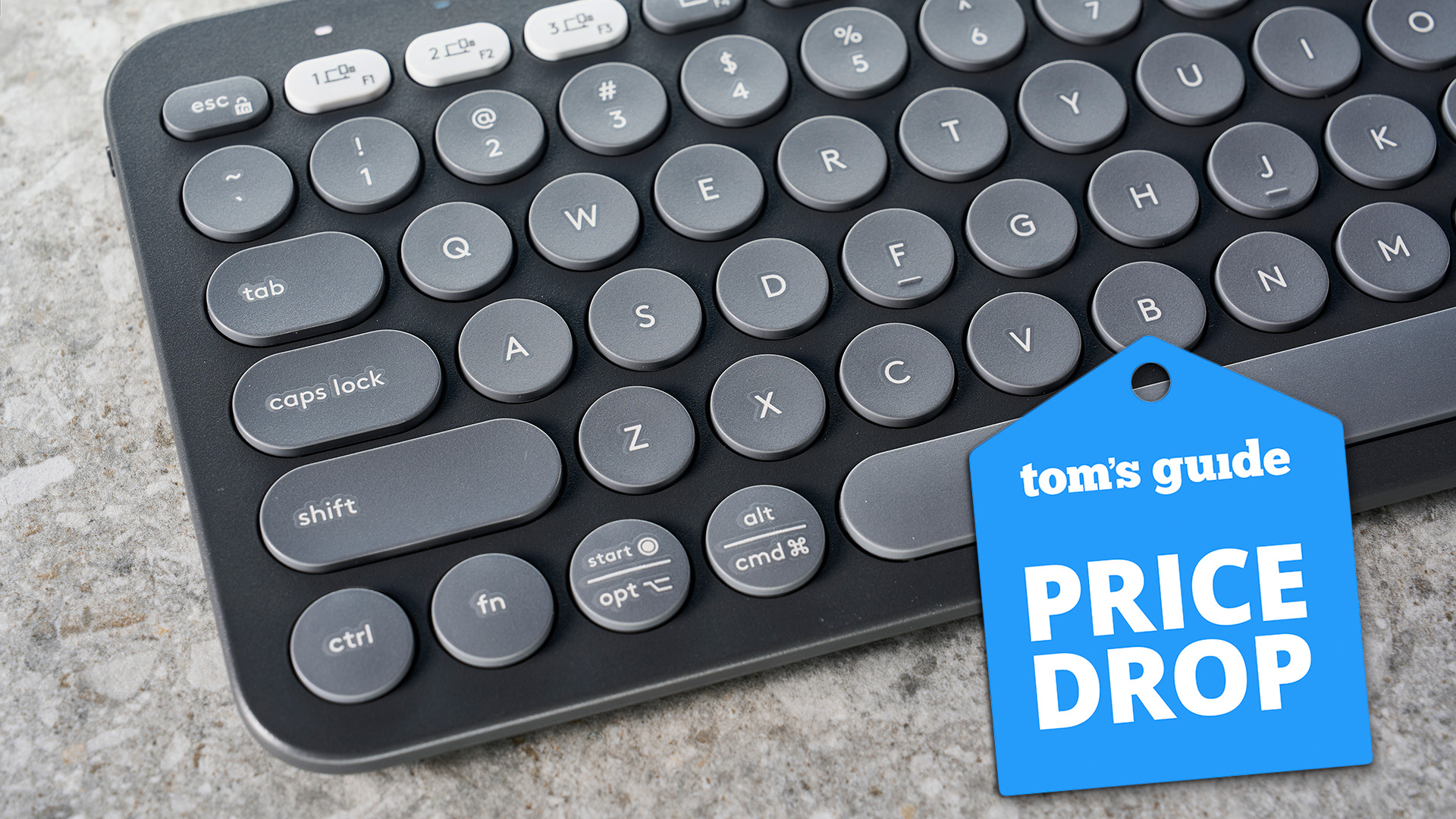 Logitech Pebble Keys K380s in graphite colorway photographed on a grey background with a deal tag