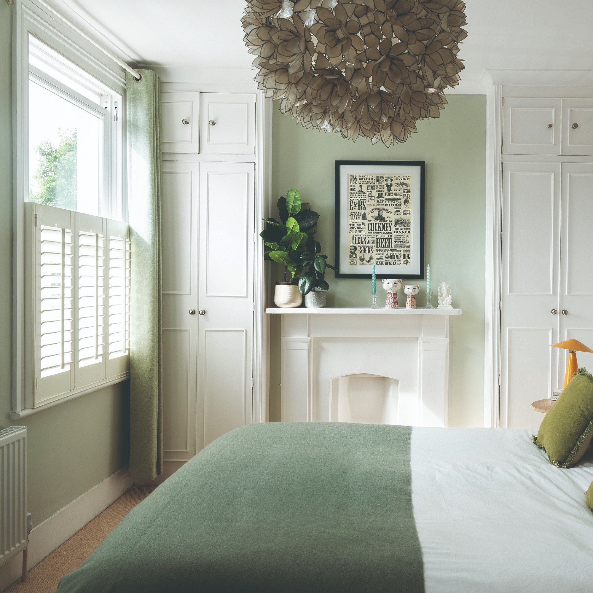 A small bedroom painted in soft green with tonal curtains and white shutters on the window
