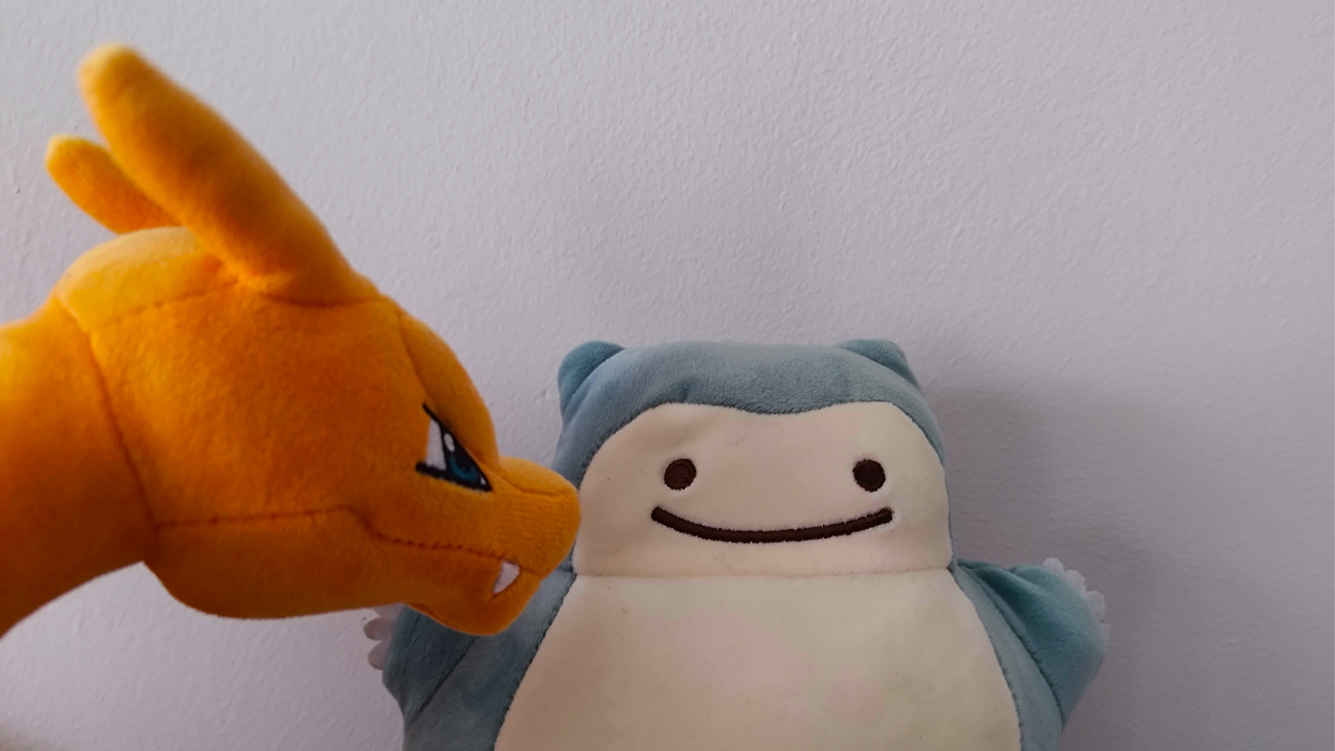 A suspicious-looking Charizard looks at a Ditto Snorlax plush